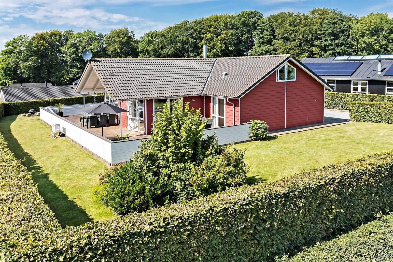 Red house with terrace and garden. Backyard with hedge and trees.