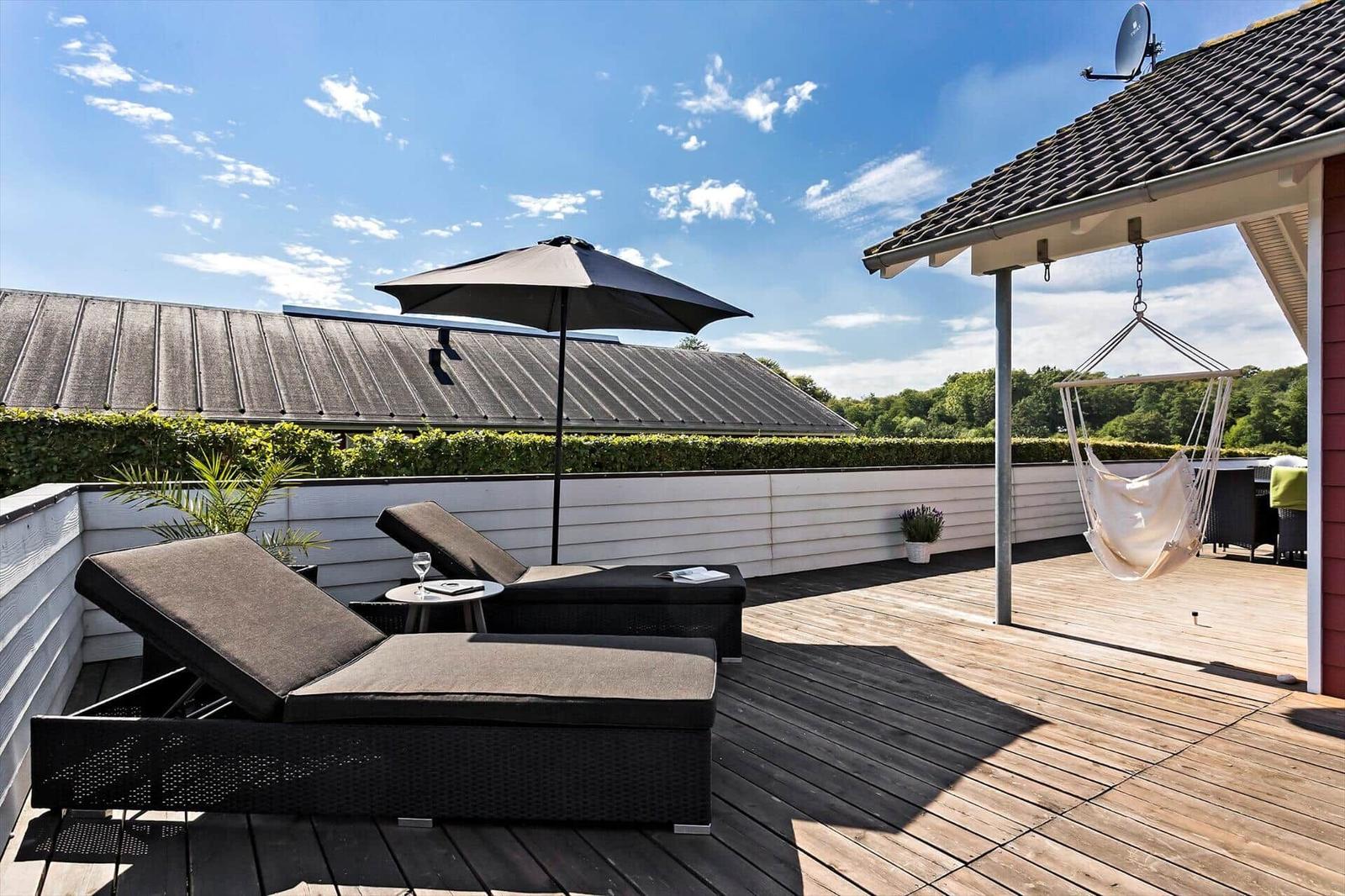 Terrace with lounge chairs, umbrella, and hammock. Wooden deck and green hedge in the background.