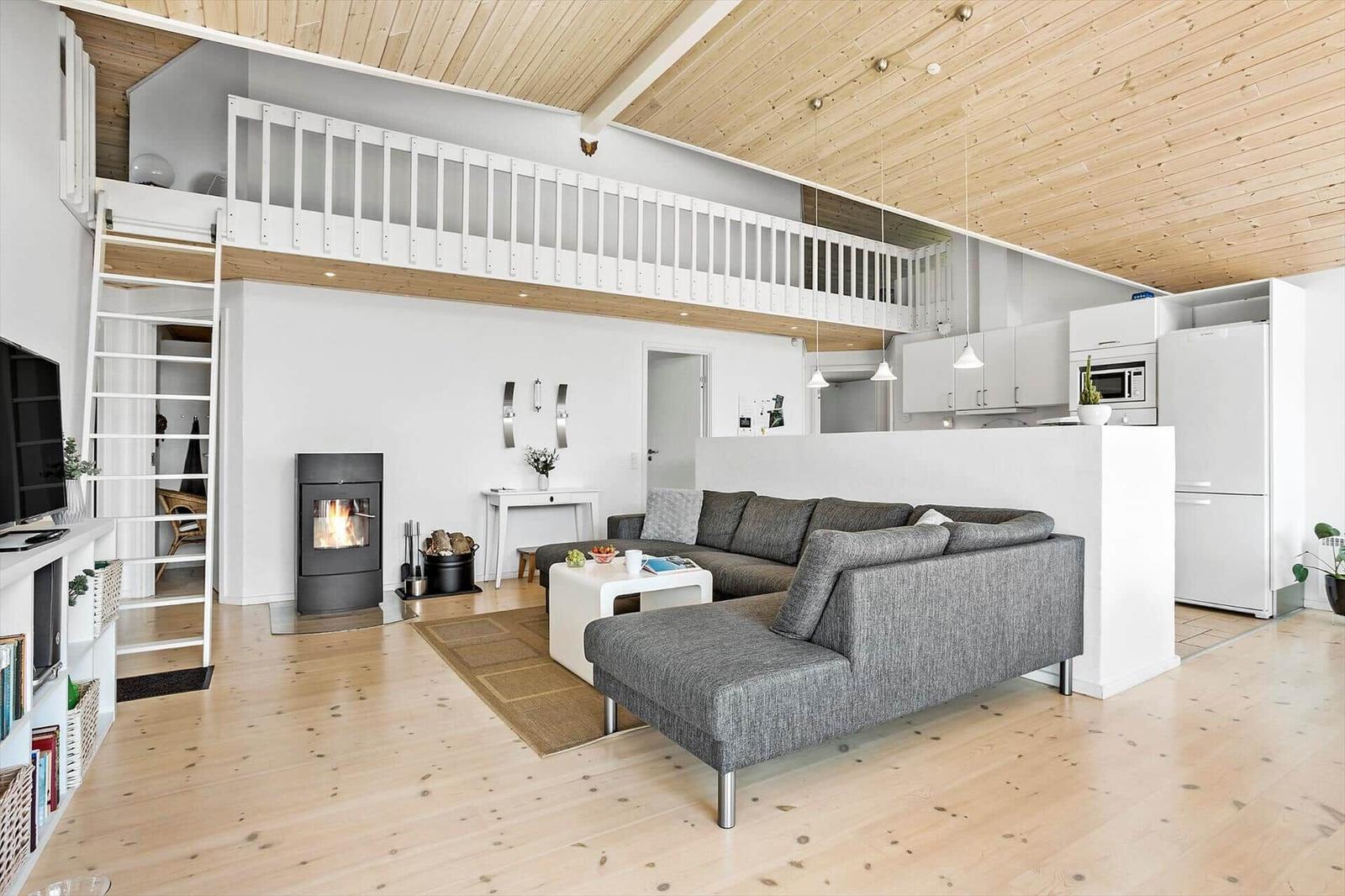 Living area with sofa, fireplace, and mezzanine. Kitchen with white cabinets.