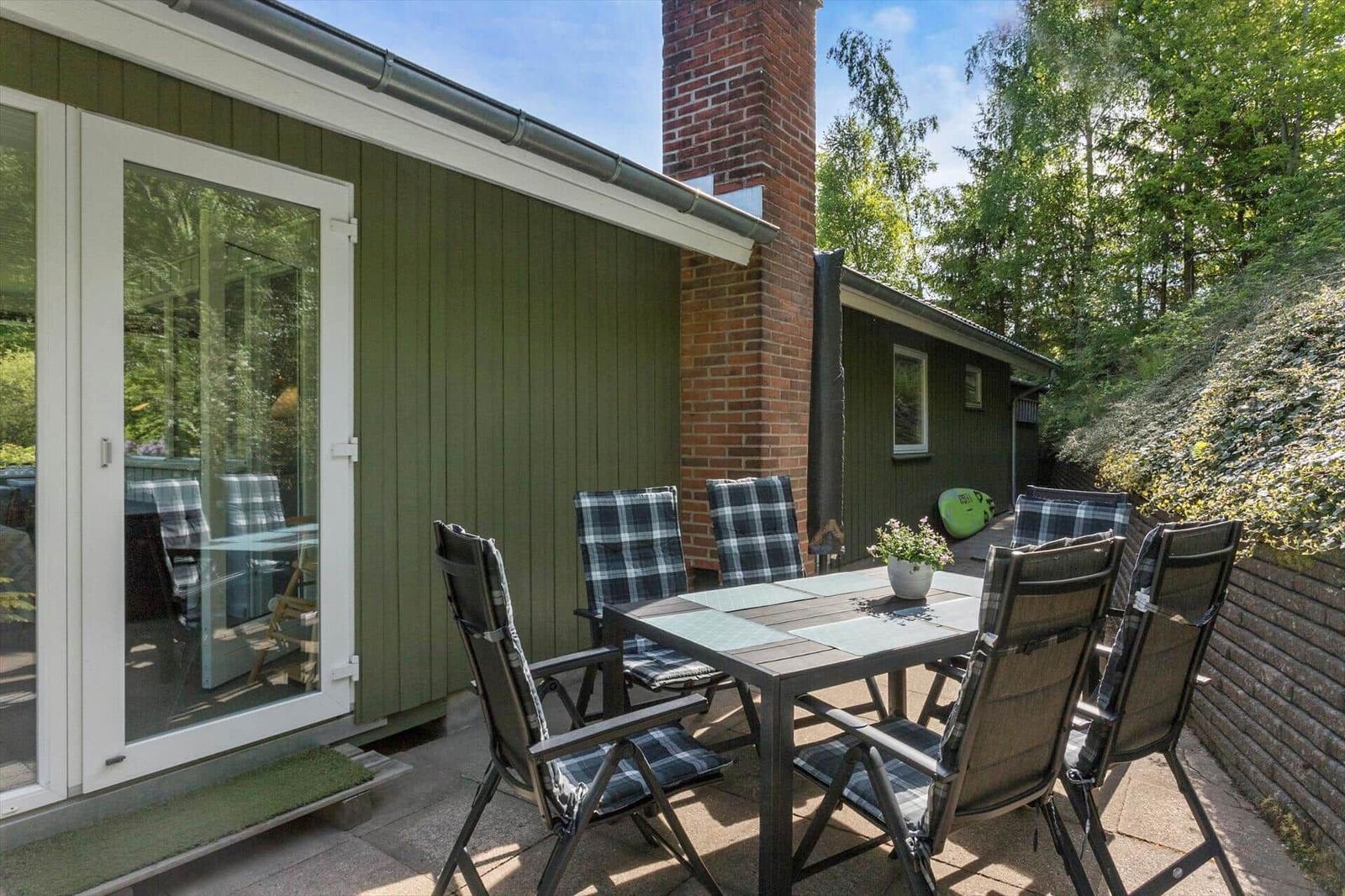 Terrace with table and chairs in front of green house with chimney.