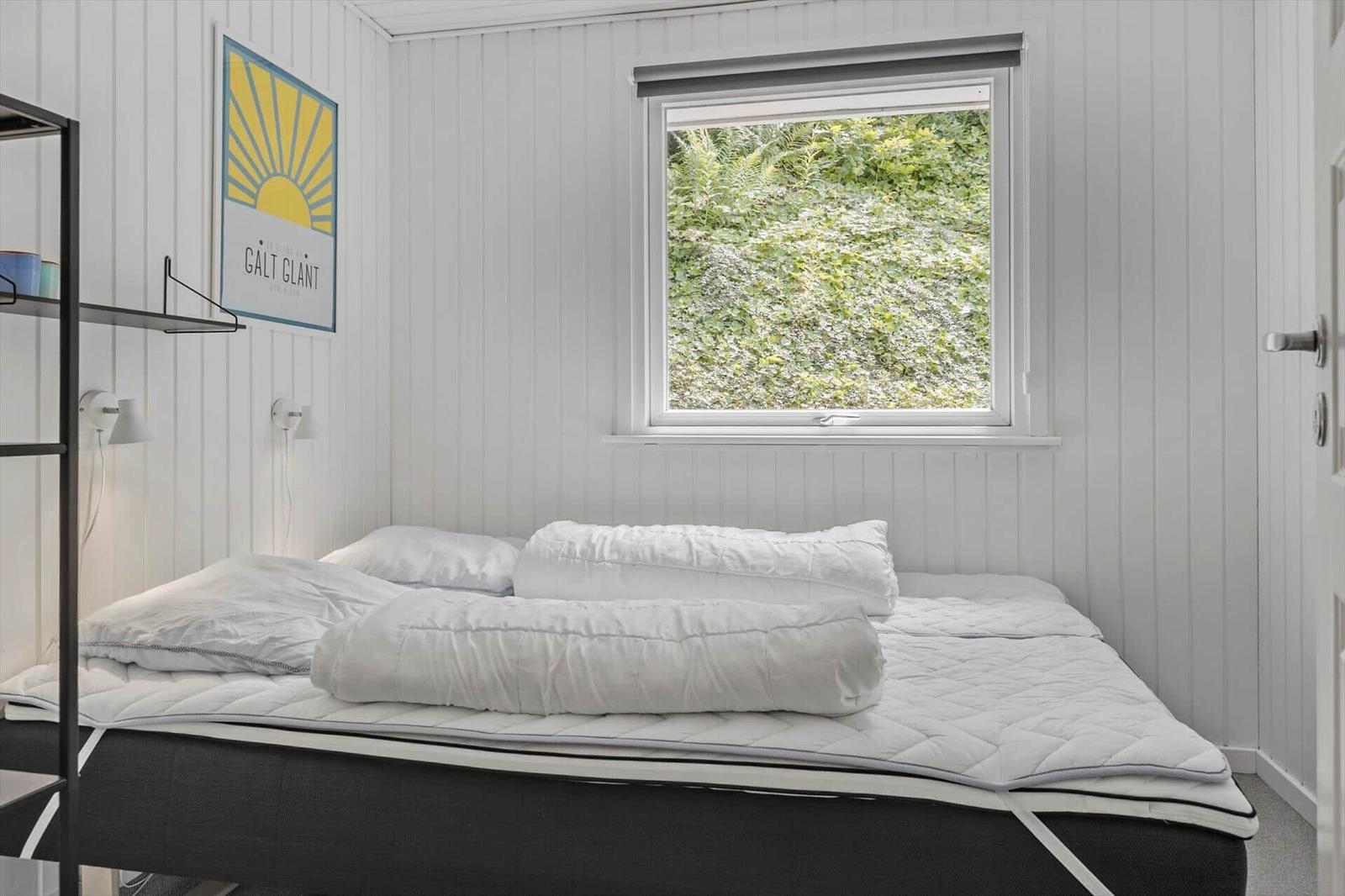 Bedroom with white bedding and window view of green plants.