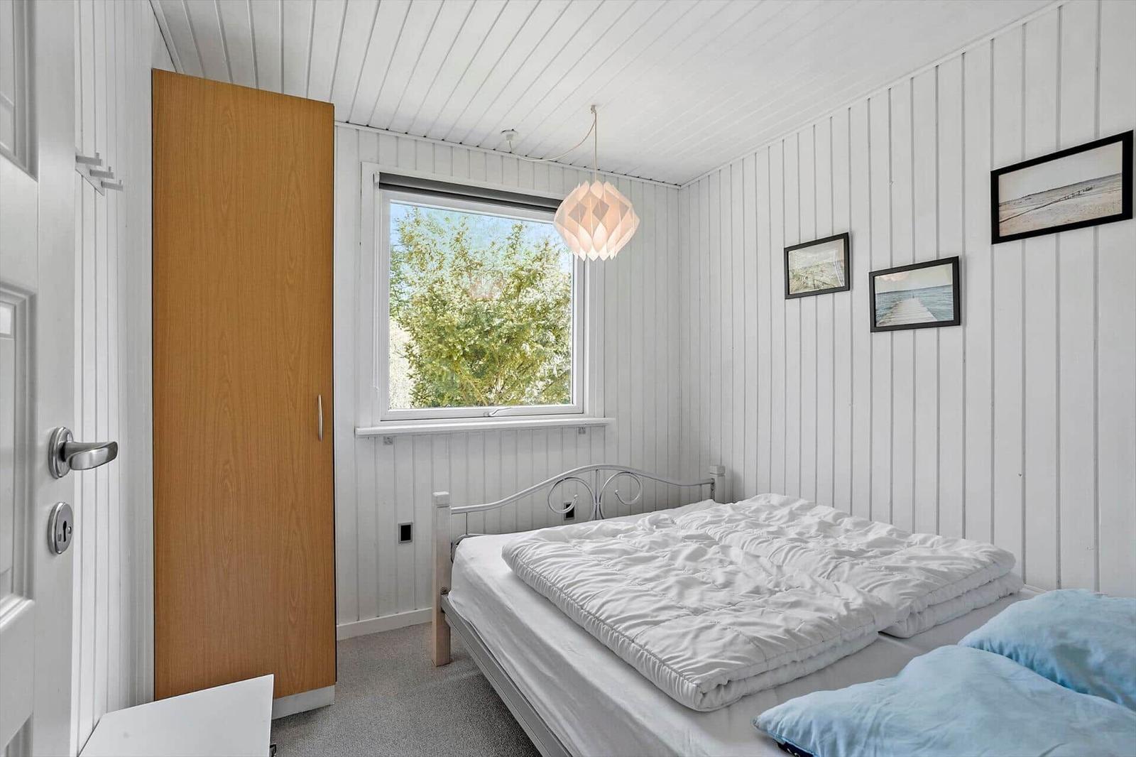 Bedroom with bed, window, and wooden wardrobe.