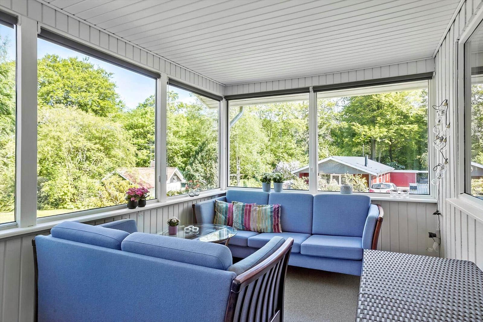 Patio with blue sofa and armchairs, large windows overlooking green trees.