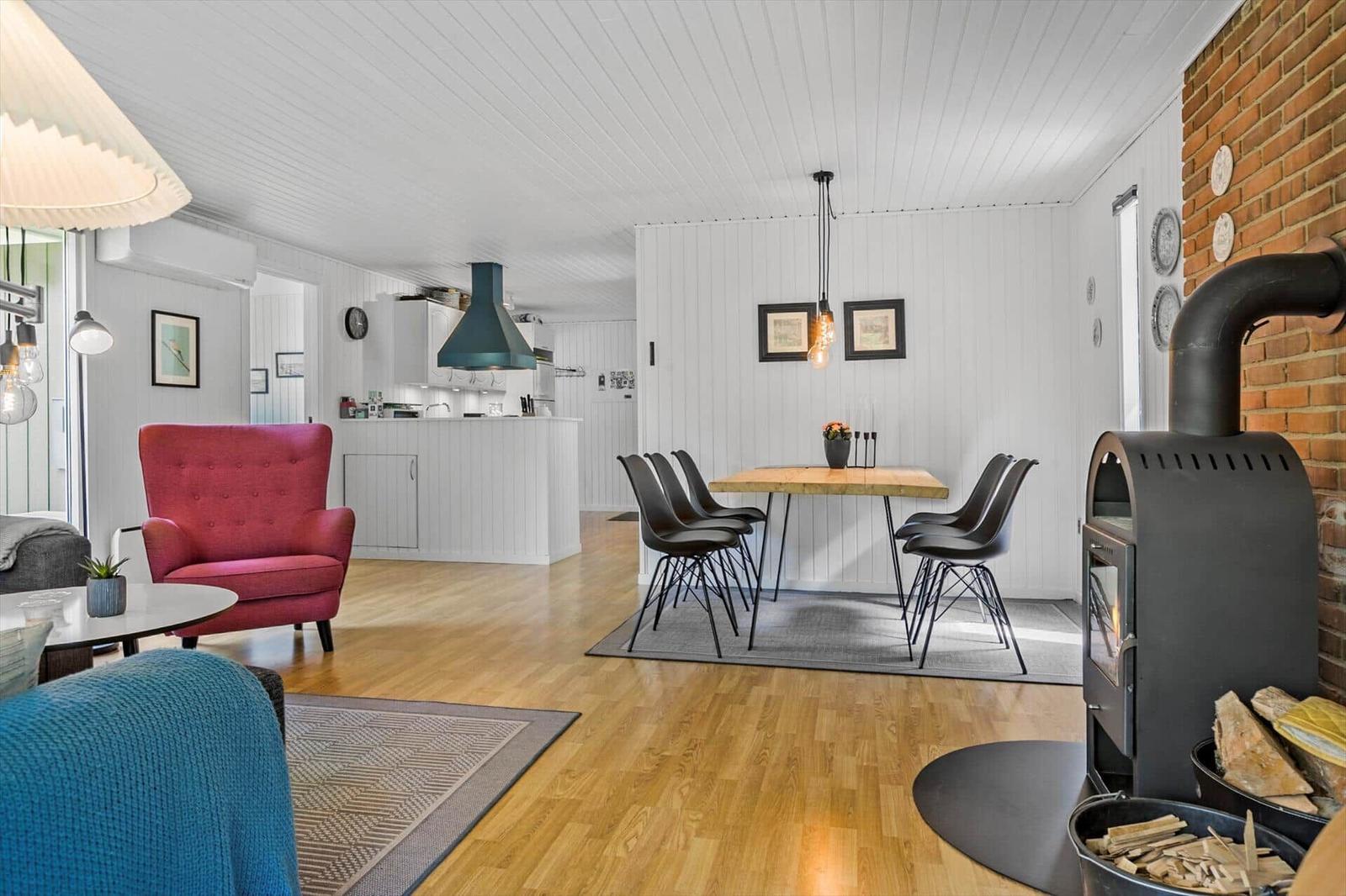 Living room with dining area, hardwood floor, and wood stove. Red seating and dining table with chairs.