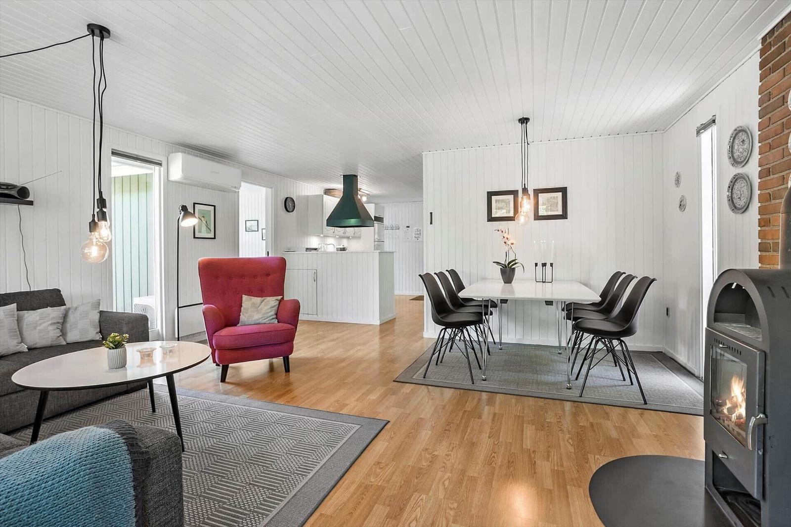 Living and dining area with wooden floor, white wall paneling, and a wood stove.