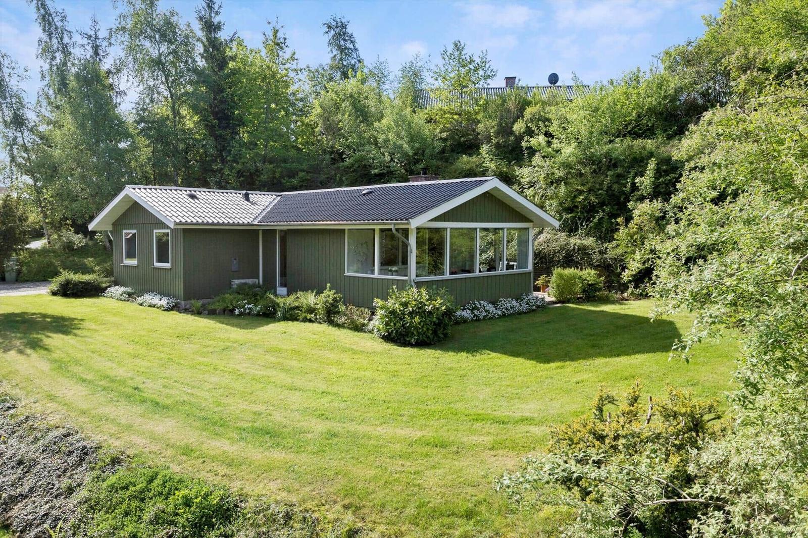A green house with a large garden surrounded by trees.