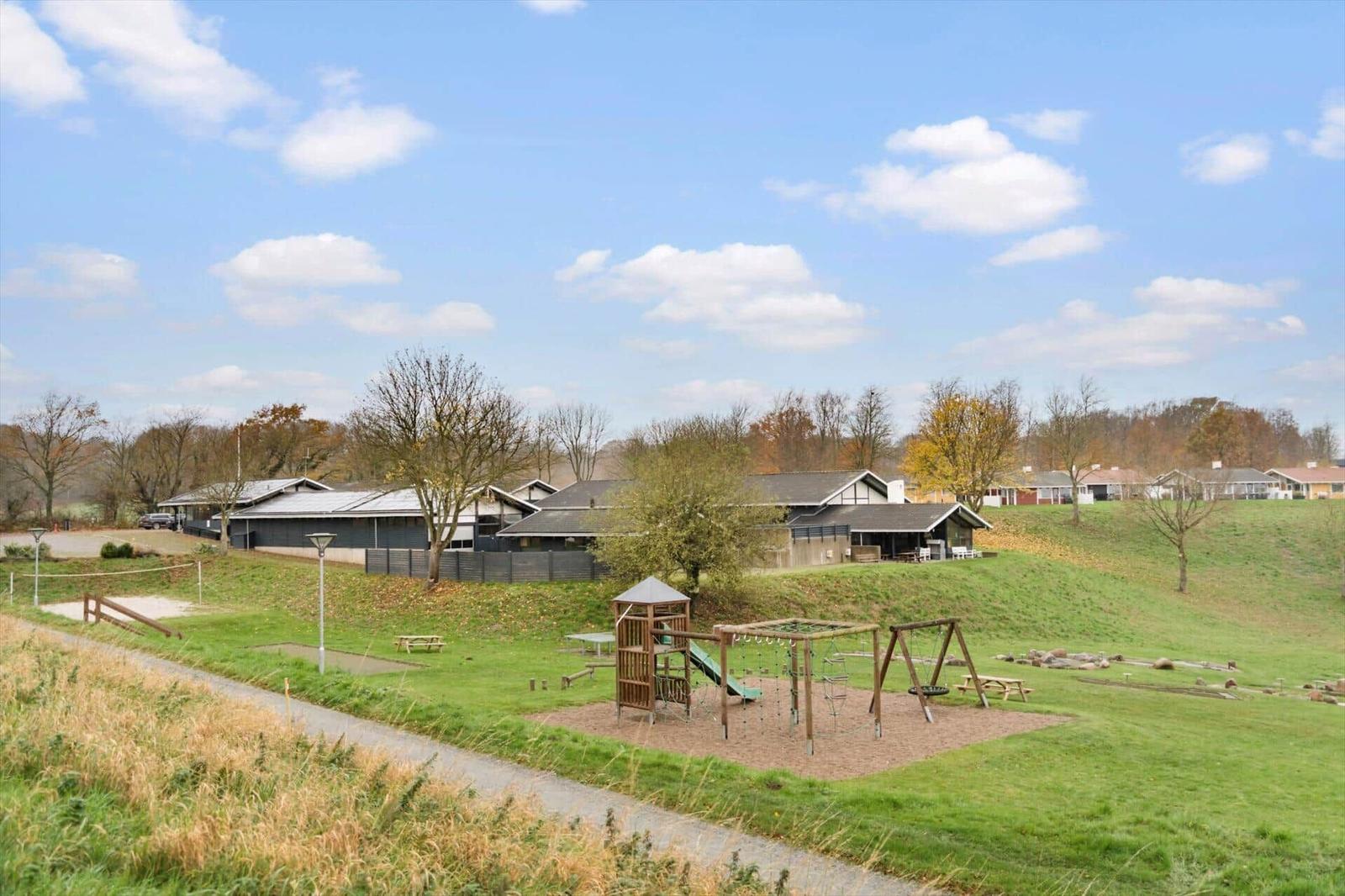 Green playground with slide and swing in front of modern houses on a lawn.