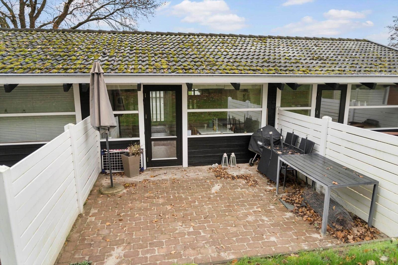 Terrace with table, chairs, and grill. Backyard with white fence and black entrance door.