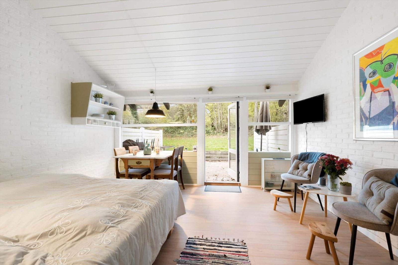 Bedroom with view of terrace and garden. White walls, wooden floor, and modern furnishings.