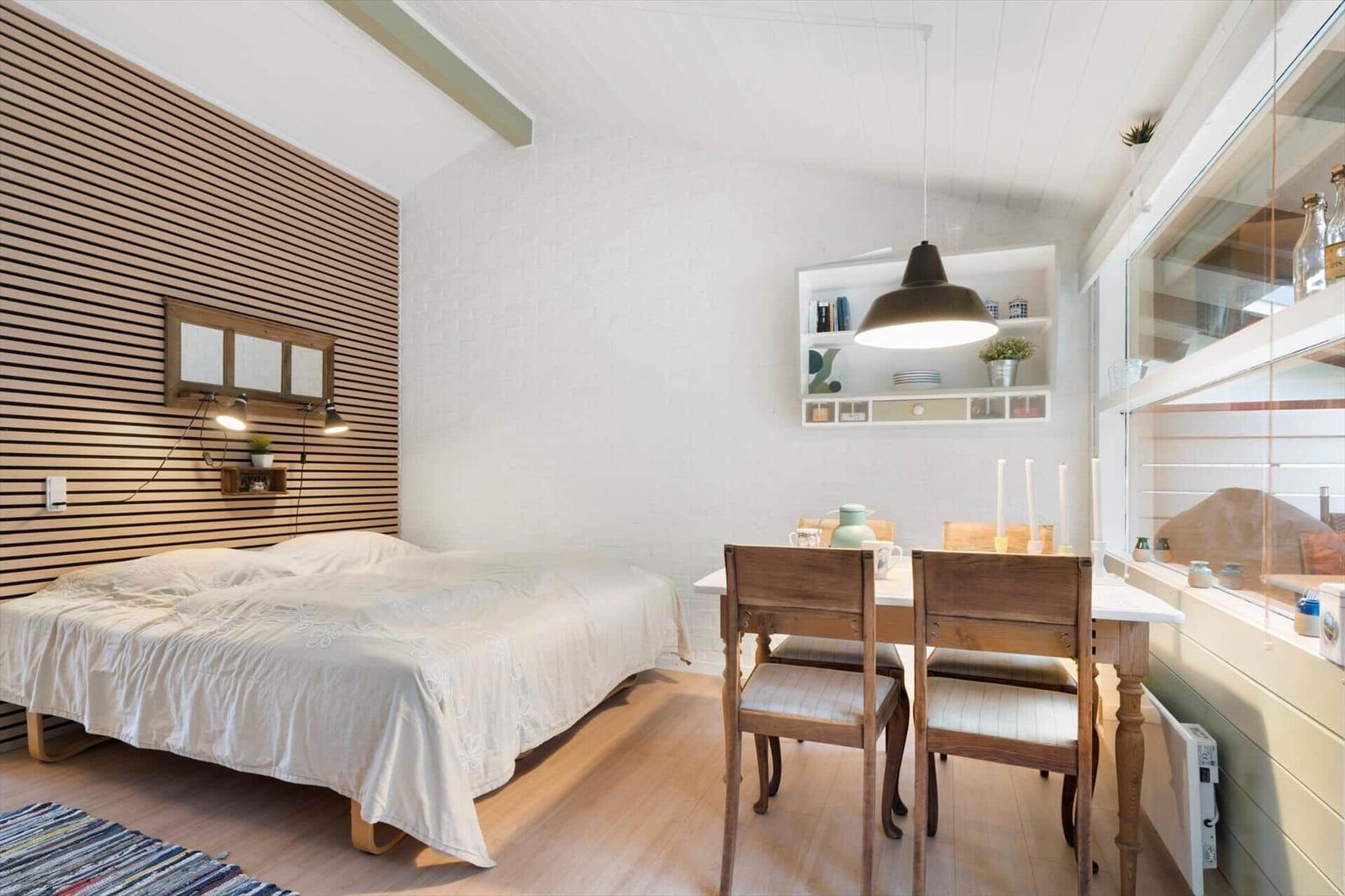 Bedroom with bed, table, and chairs. Wooden wall, white walls and ceiling.