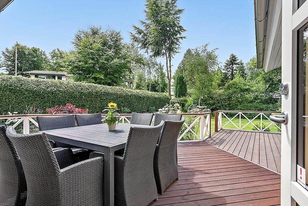 Deck with table and chairs, surrounded by green hedges and trees.