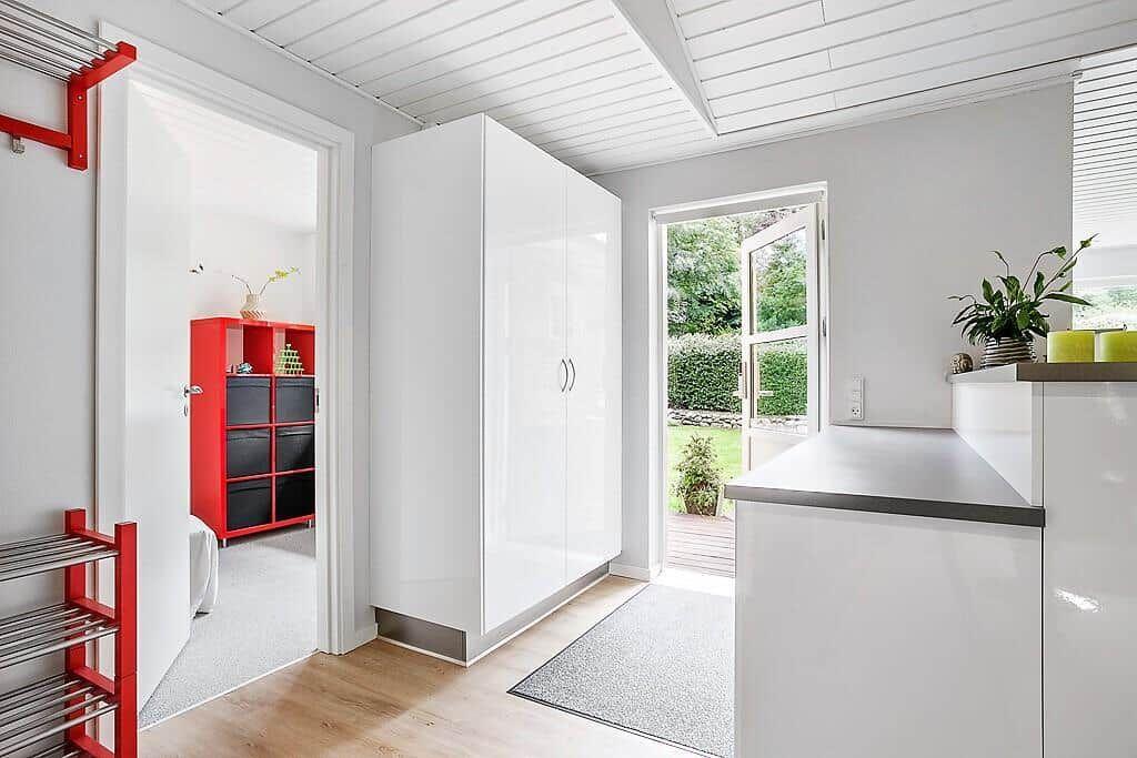 Entrance area with white cabinet and red coat rack. Passage to a room with red shelving.