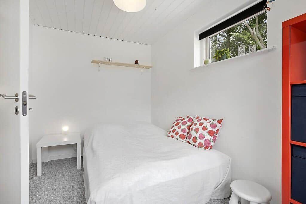 Bedroom with white bed, red cabinet, and window with view of trees.