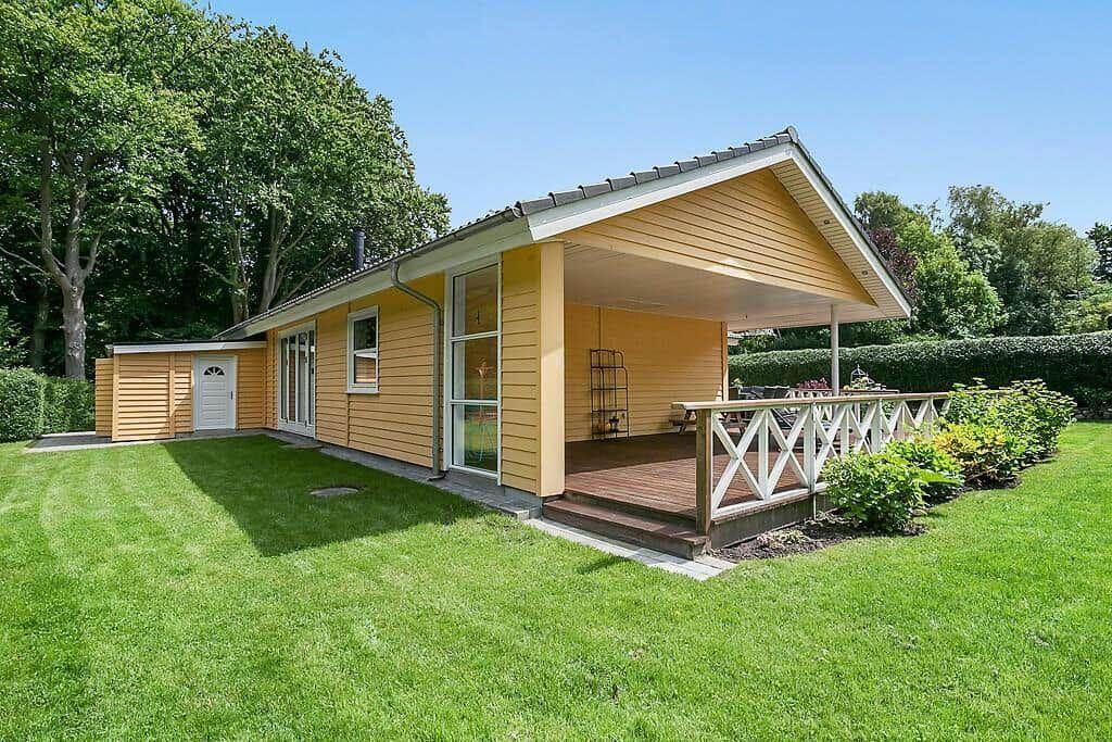 A yellow house with a porch and garden. Wooden terrace with white railings.