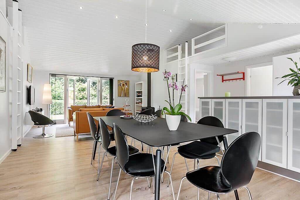 Dining area with black tabletop and black chairs. Background: living area with brown sofa and glass doors.