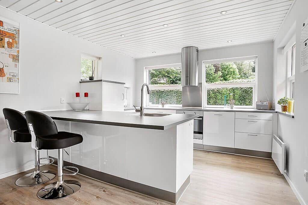 Modern kitchen with island, black bar stools, and windows to the garden.