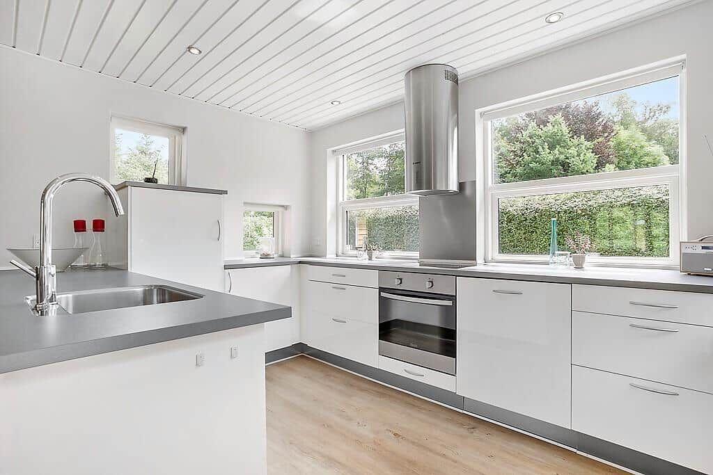 Modern kitchen with white cabinets, stainless steel appliances, and large windows overlooking greenery.