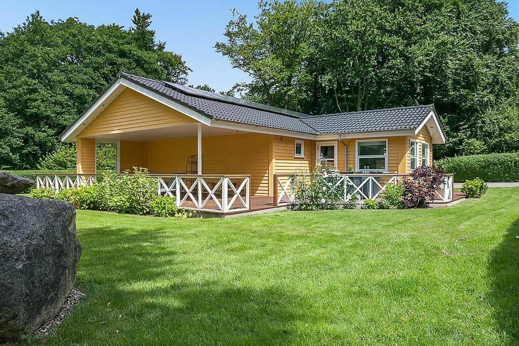 Yellow vacation home with balcony and green lawn. Surrounded by trees and shrubs.