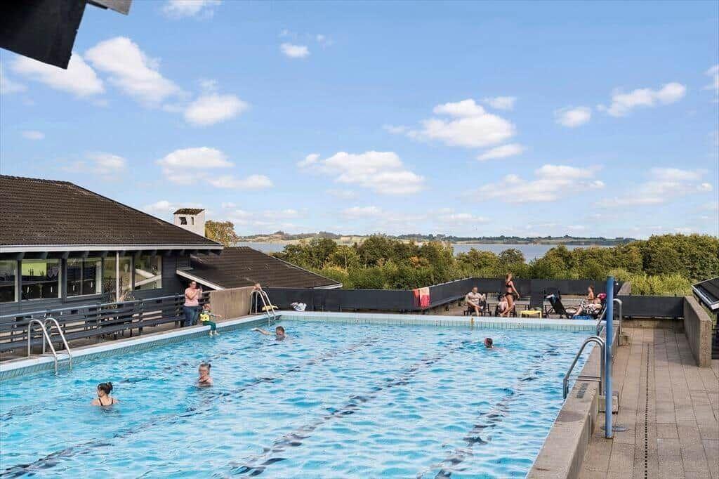 Outdoor pool with swimmers and view of water and trees.
