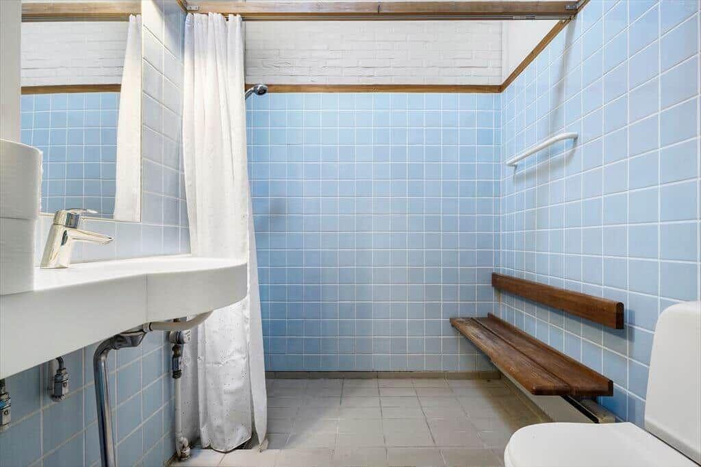 Bathroom with blue tiles, sink, shower, and wooden bench.