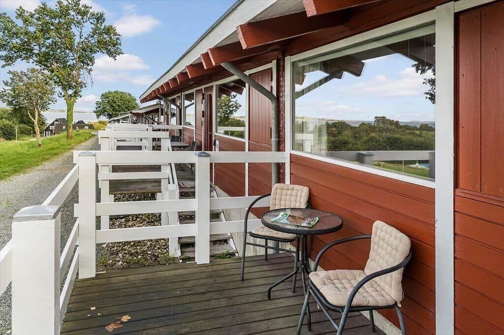Deck with table and two chairs beside red wooden house overlooking landscape.