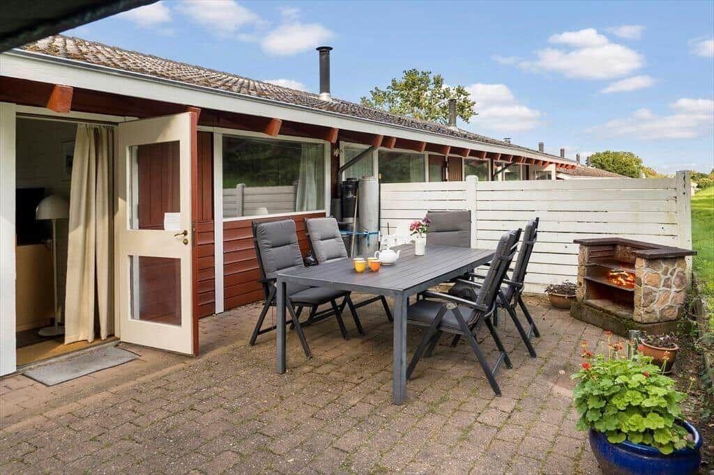 Patio with table, chairs, and grill. Backyard with white fence and garden.
