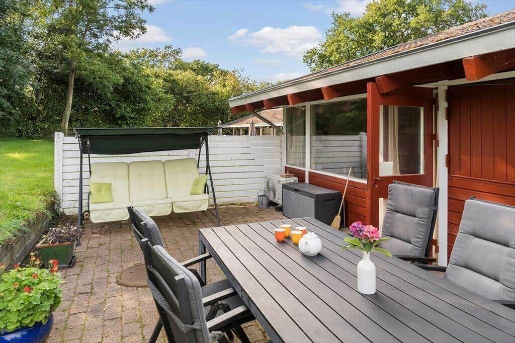 Terrace with table, chairs, and swing under a green sky.