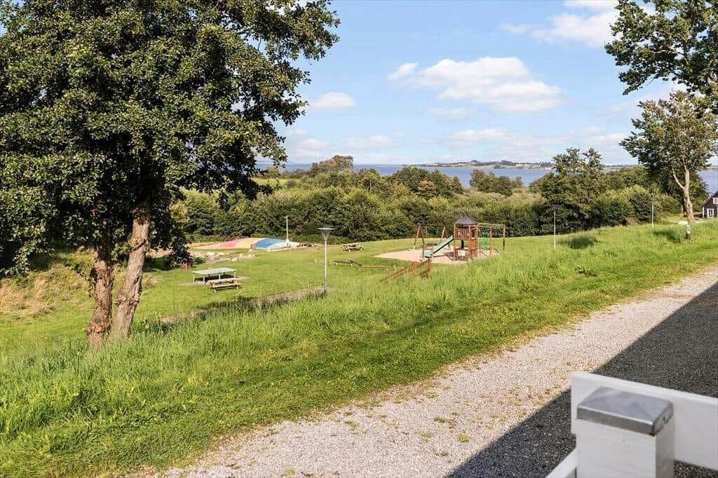 Green playground with slide and table under trees. View of water and forest.