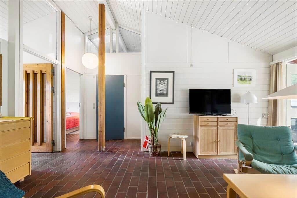 Living room with TV, plant, and seating. Wooden floor and white walls.