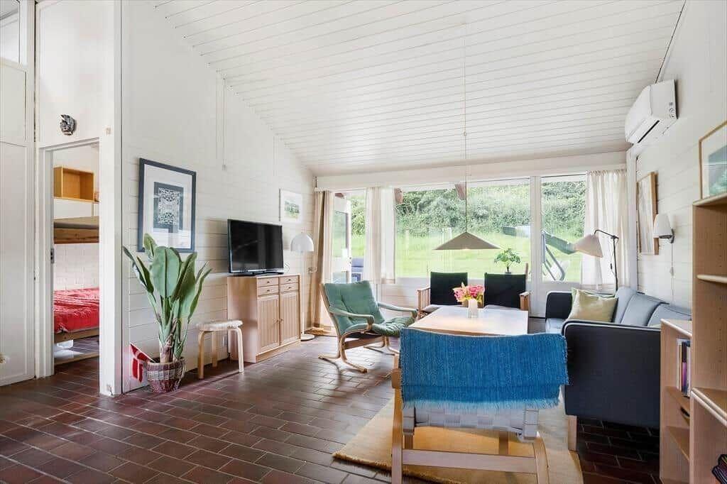 Living room with dining area, TV, and view of greenery. Bedroom in the background.