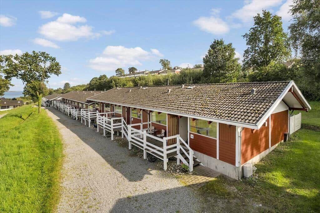 Row of wooden houses with white porches and tiled roofs along a grass strip.