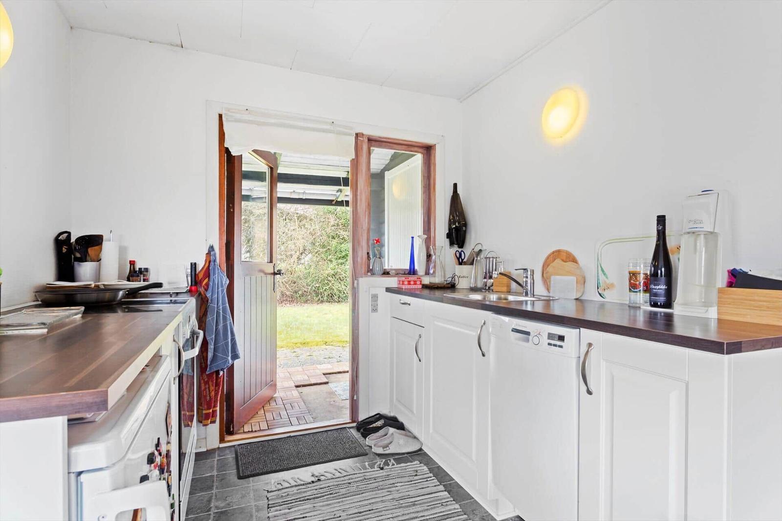 Kitchen with white cabinets, dark countertop, and door to the garden.