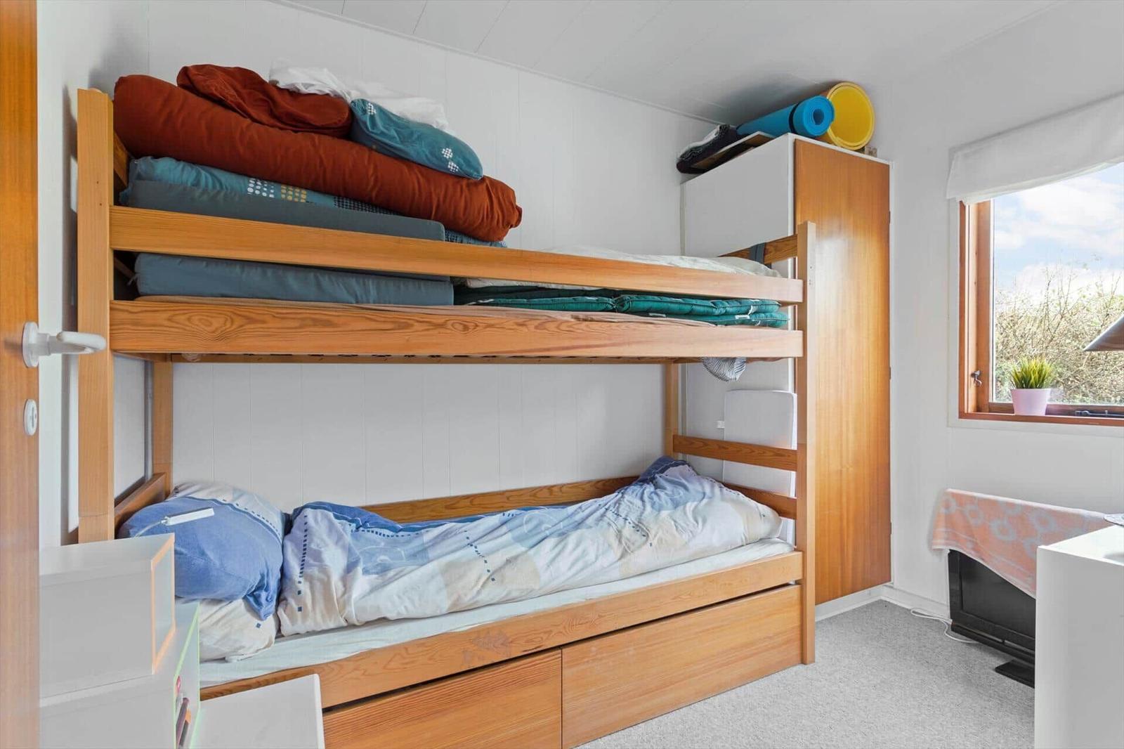 Room with bunk bed, wardrobe, and window with view of outside area.