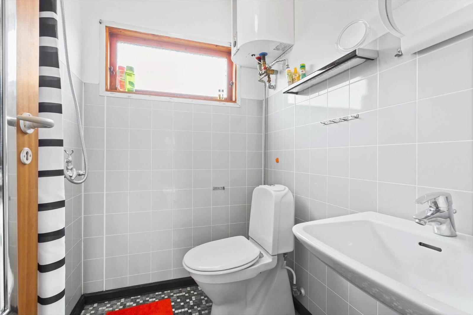 Bathroom with toilet, sink, and shower. Window with wooden frame.