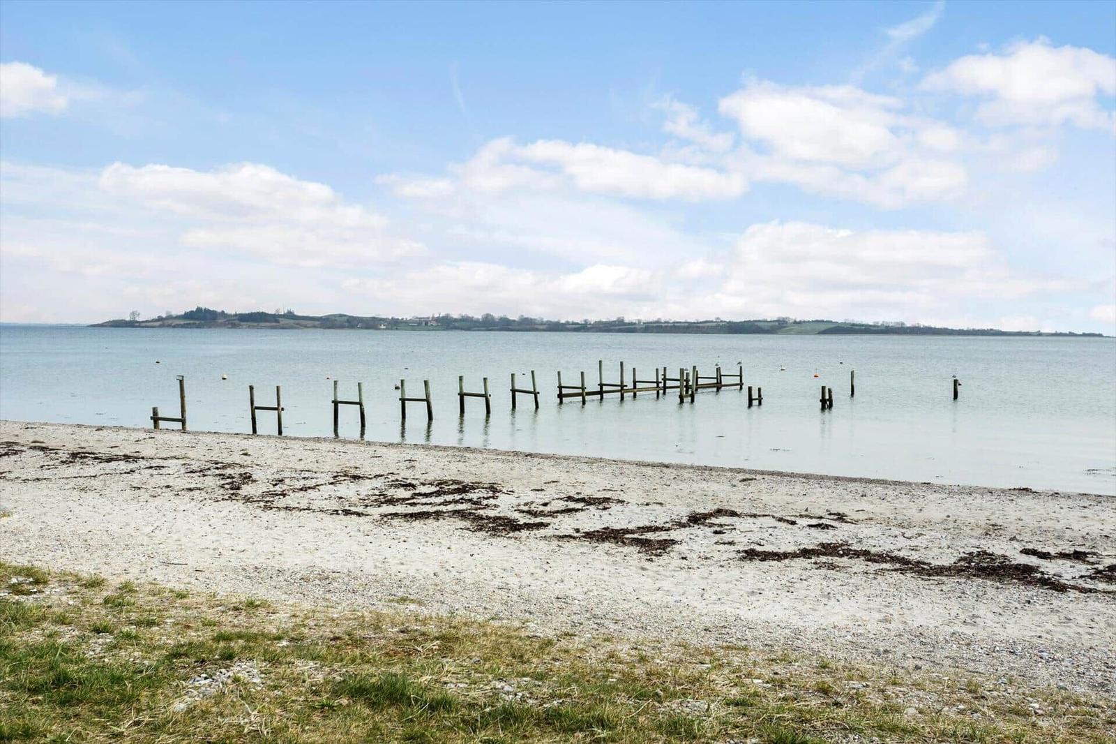 Beach with wooden posts in water and island in background under blue sky.