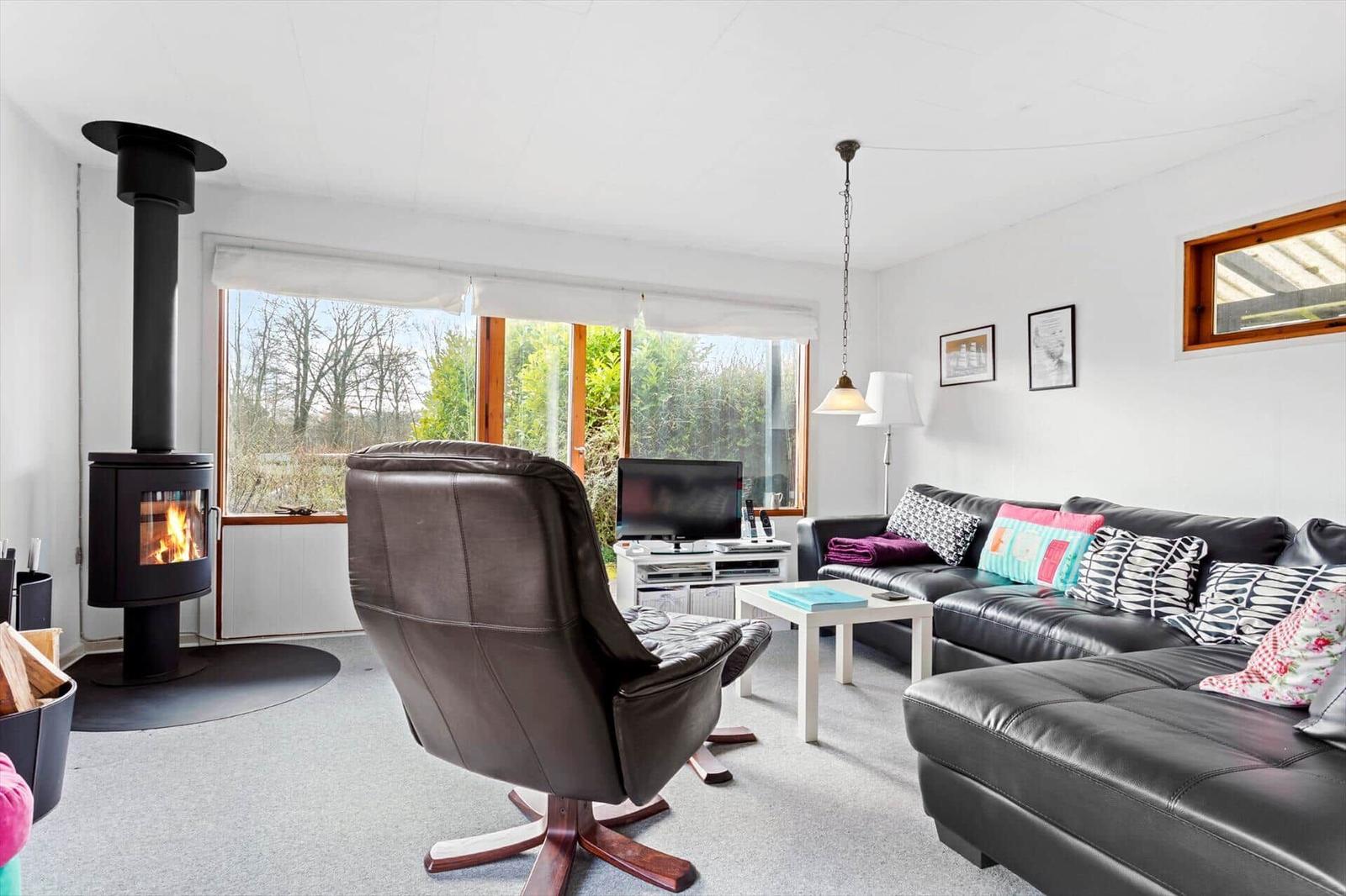 Living room with sofa, chair, and wood-burning stove. Large windows and table.
