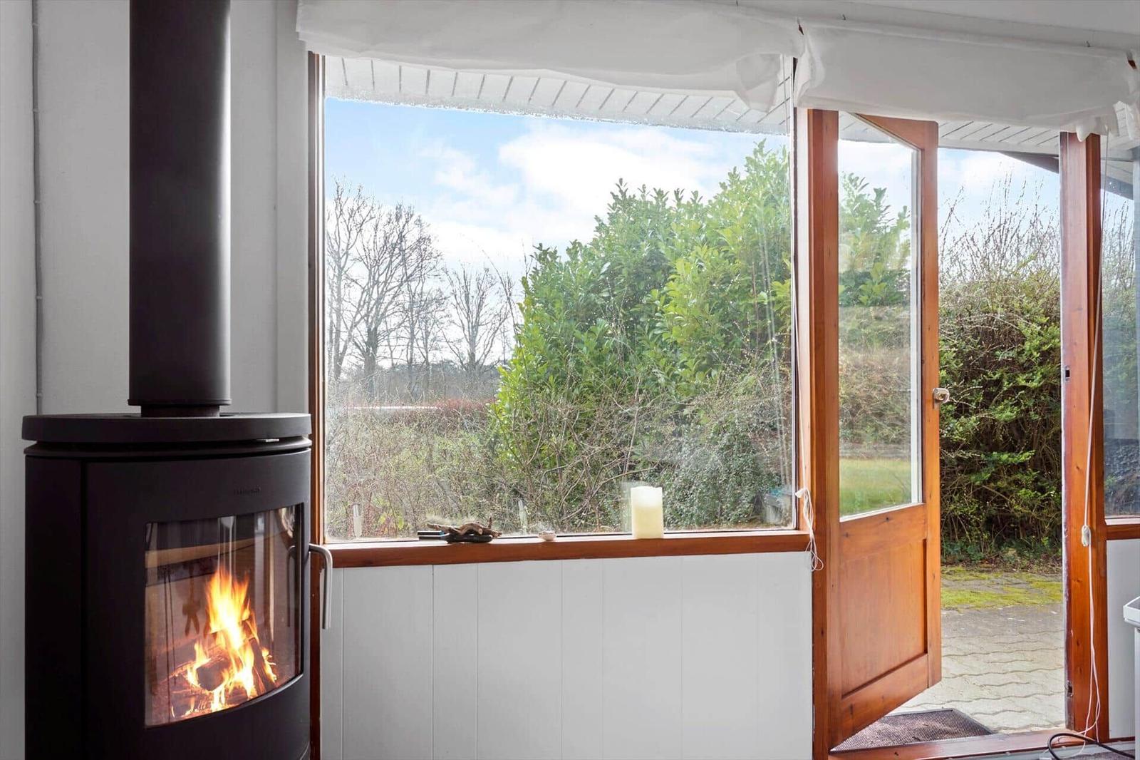 A wood stove stands before a large window with a view of a garden.