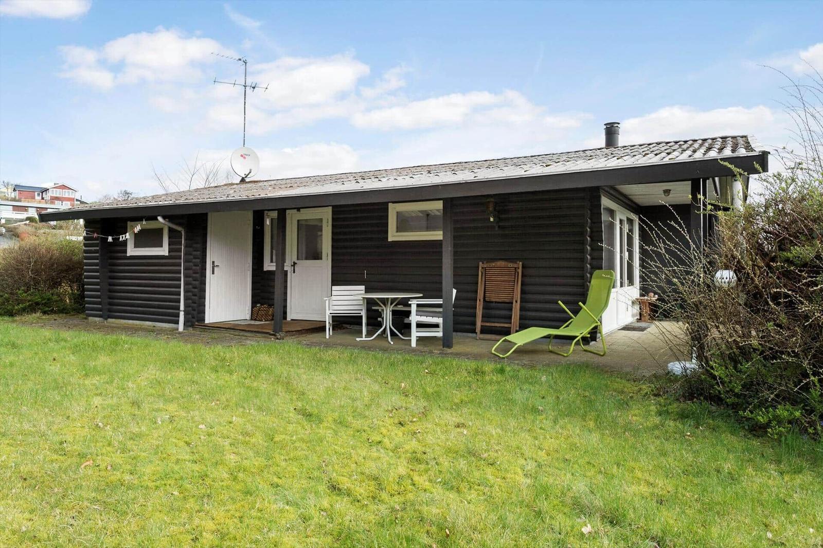 A black wooden house with a terrace, green lounge chair, and white table.