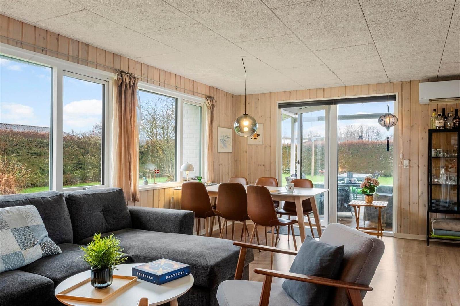 Living and dining area with sofa, table and chairs. Large windows and glass door to the garden.