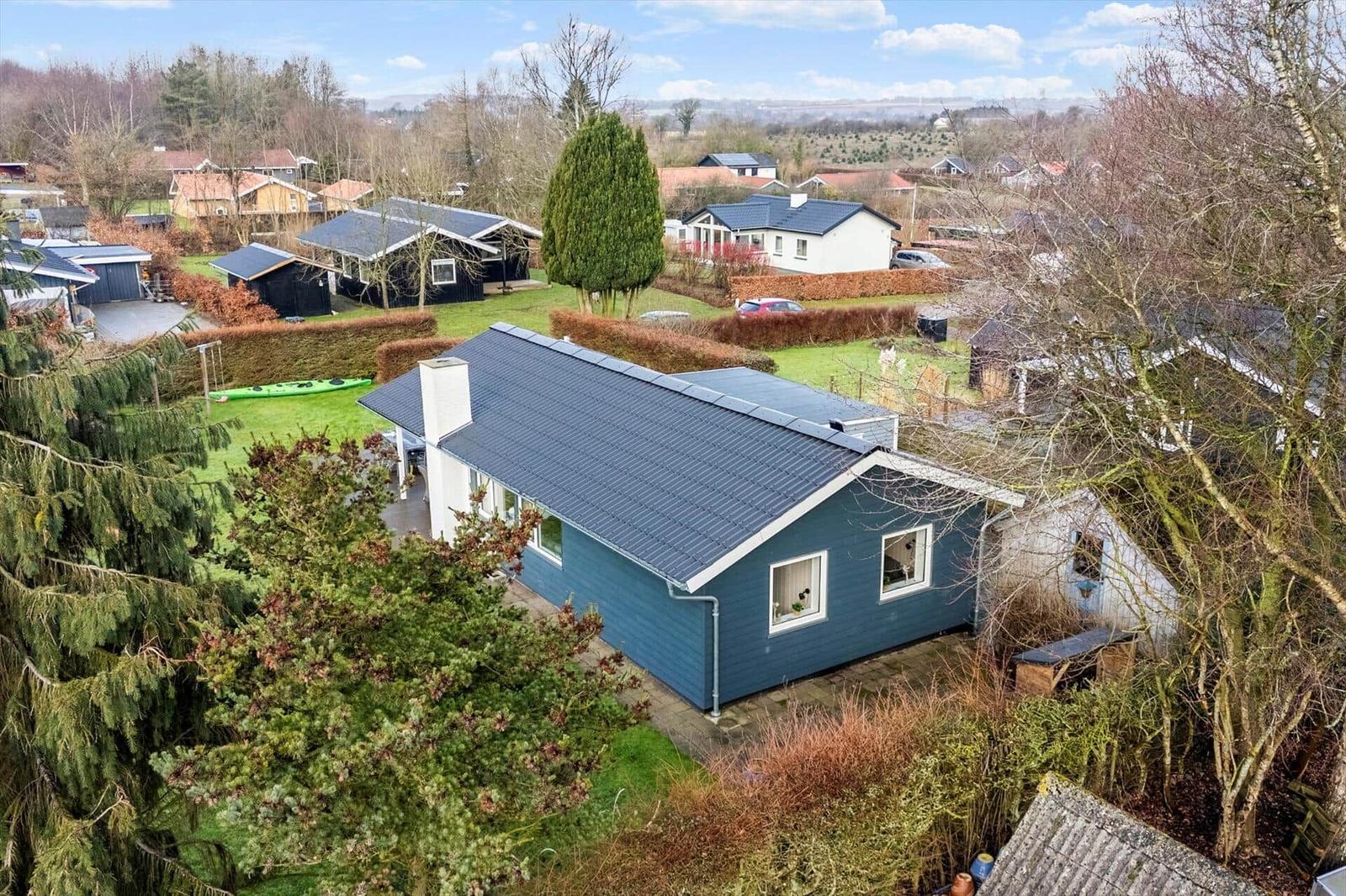 A blue house with a dark roof and garden in the background.
