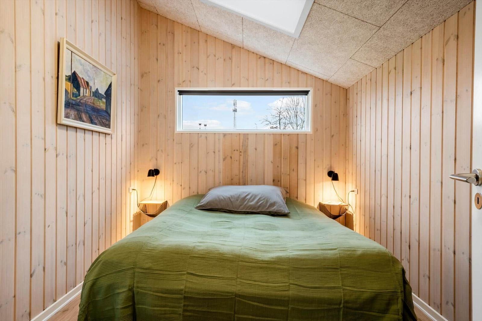 Bedroom with wooden walls, bed, and window. Ceiling with skylight.