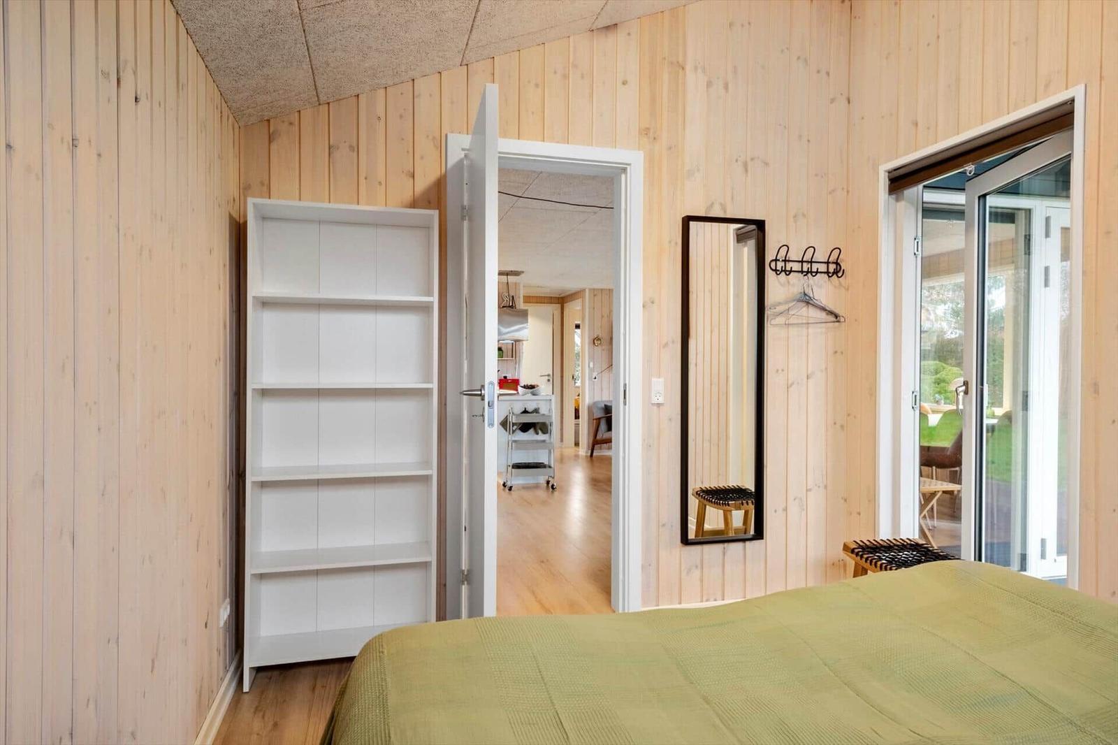 Bedroom with wooden walls, bed, mirror, and door to hallway.