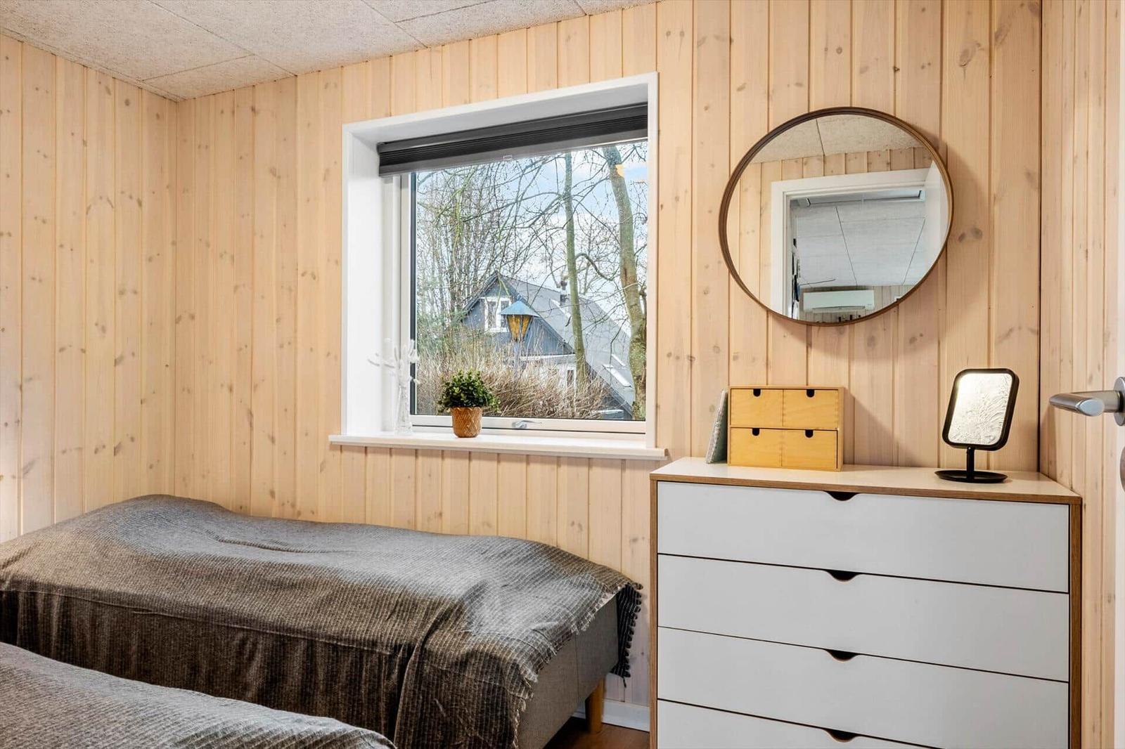 Bedroom with wood walls, window, mirror, and dresser.