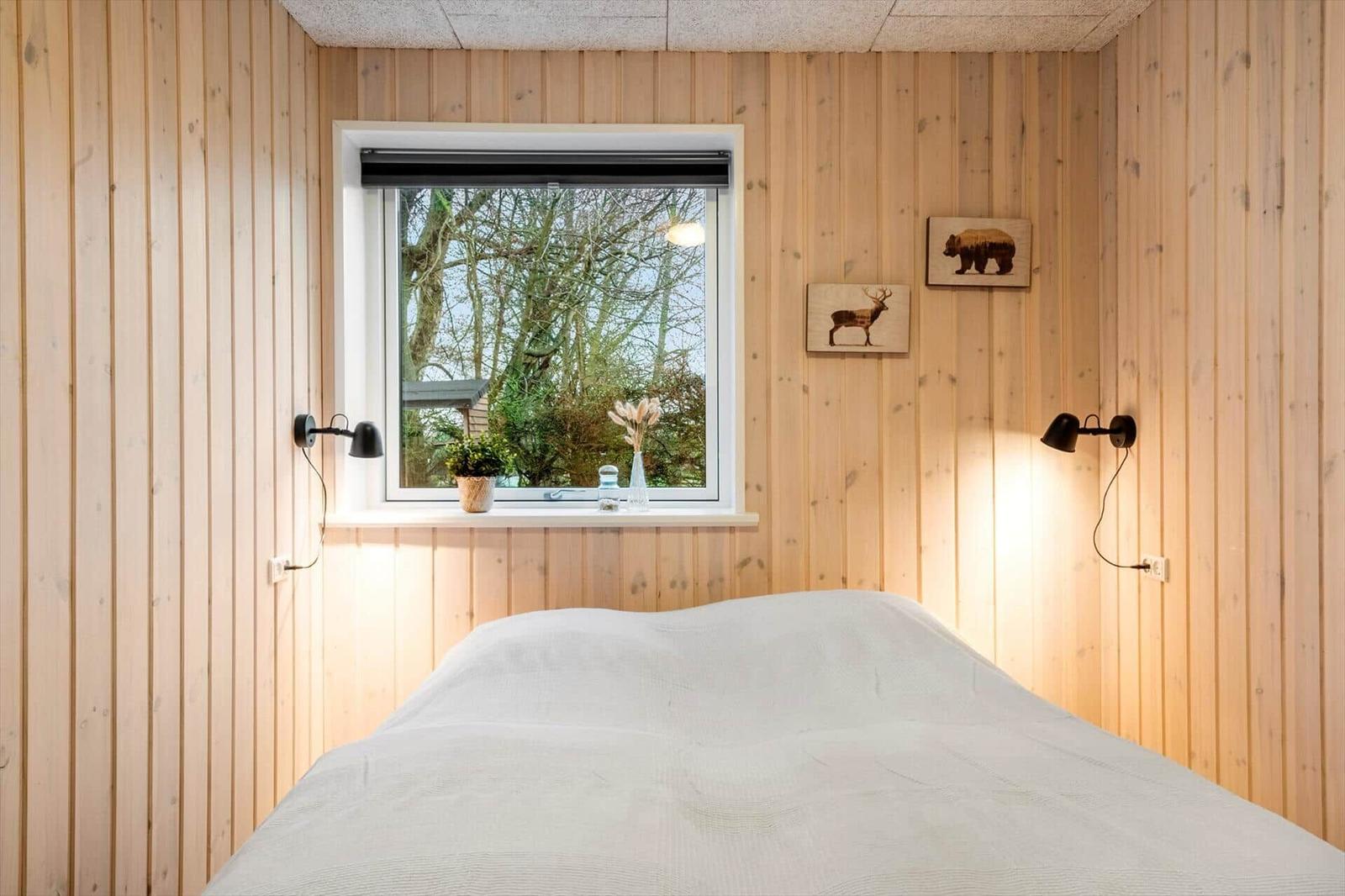 Bedroom with wooden walls, window, and bed. Animal pictures hang on the walls.