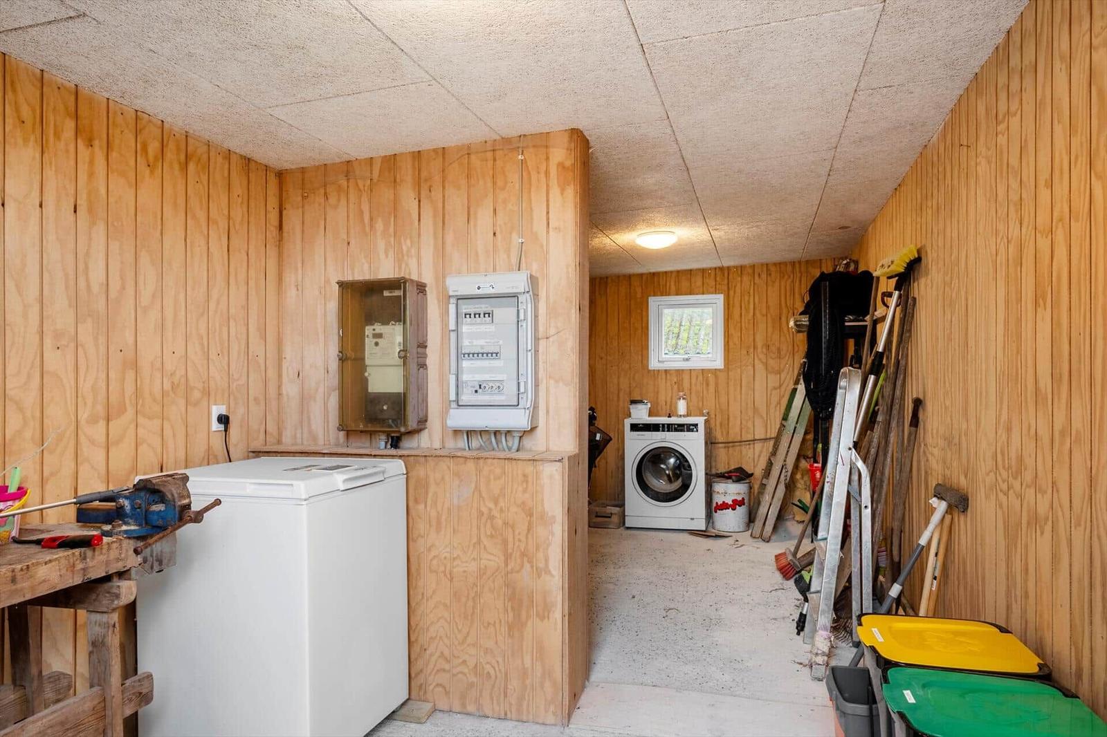 Room with washing machine, tools, and trash bins against walls.