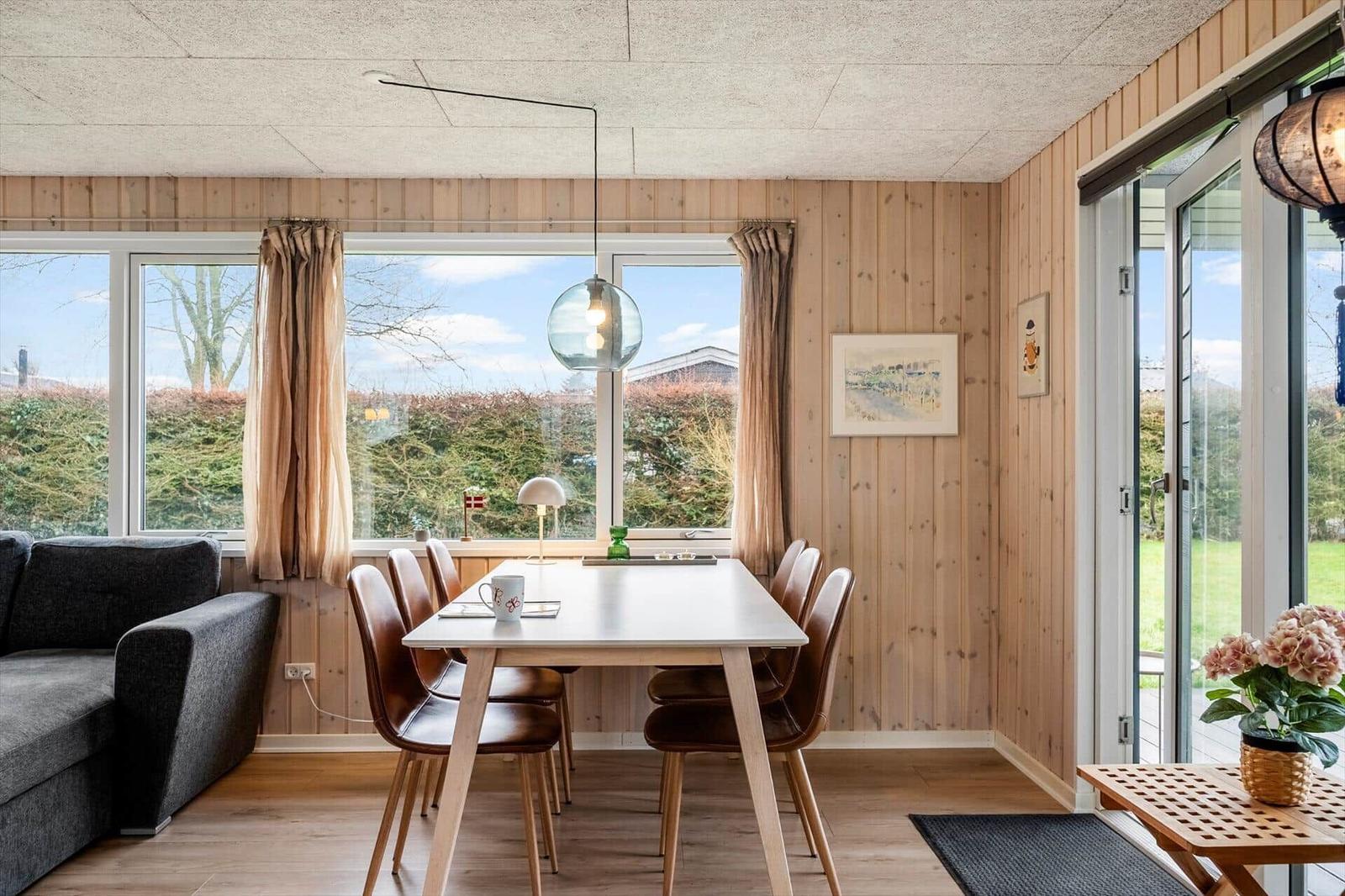 Dining area with table, chairs, and sofa. Wooden walls, large windows, and glass door.