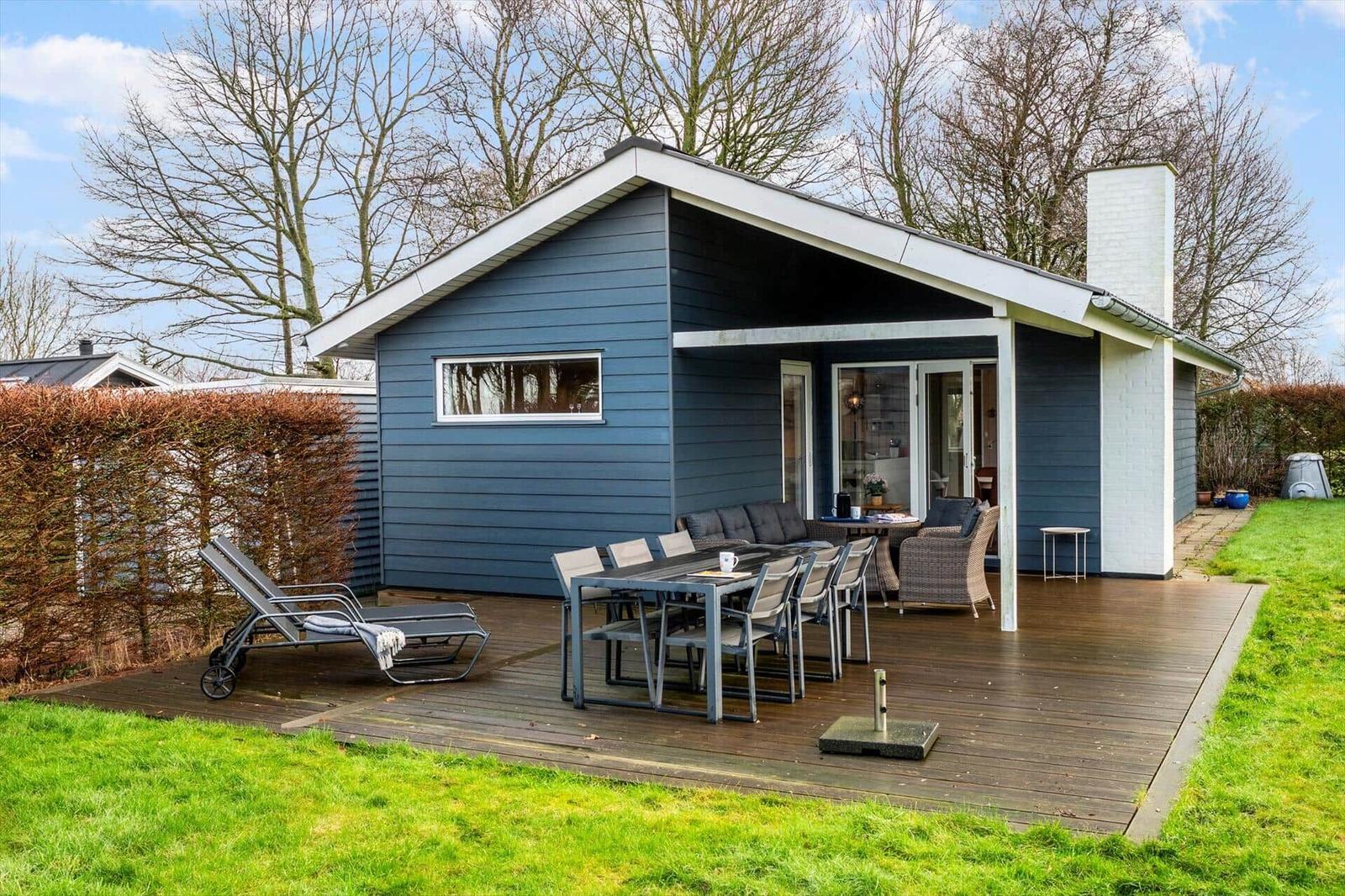 Blue wooden cabin with terrace, garden furniture, and barbecue area.