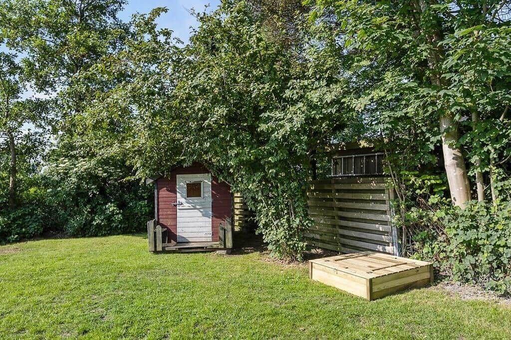Red wooden shed with white door in garden under trees.
