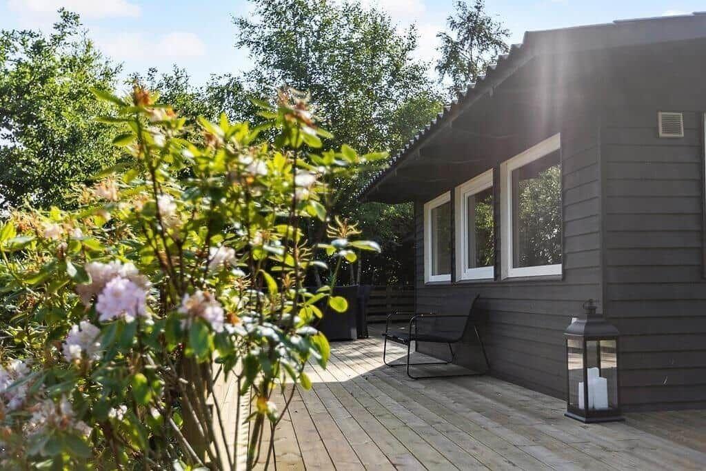 Wooden terrace with seating area in front of a dark gray house with windows.