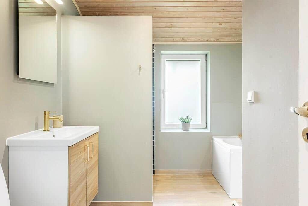 Bathroom with sink, mirror, and bathtub. Wooden ceiling and window with plant.
